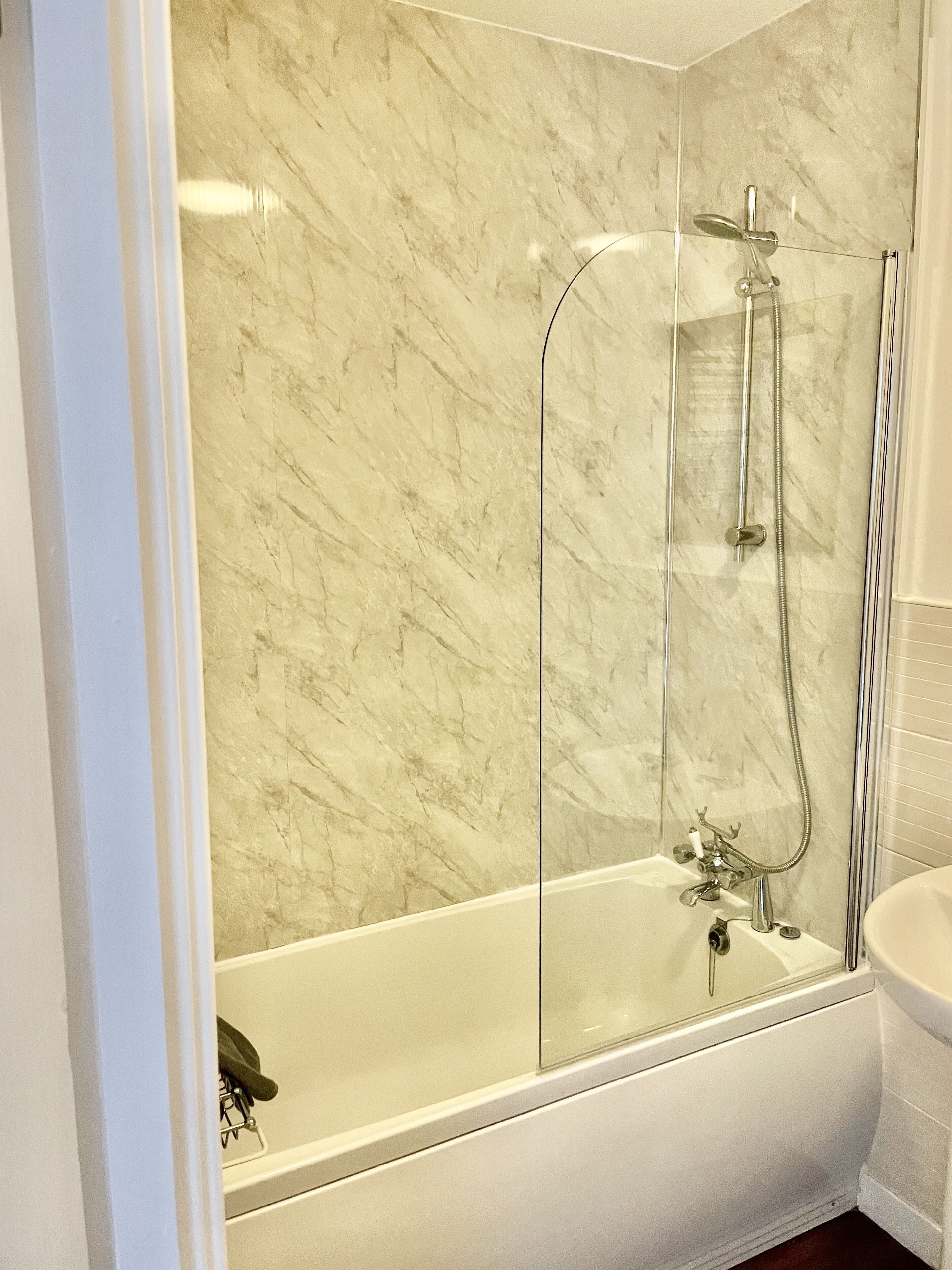 A modern bathroom with a glass-enclosed shower, a white bathtub, and a marble wall.