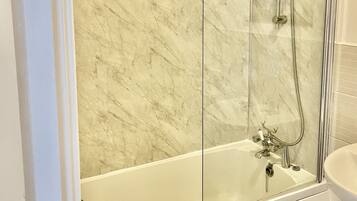 A modern bathroom with a glass-enclosed shower, a white bathtub, and a marble wall.