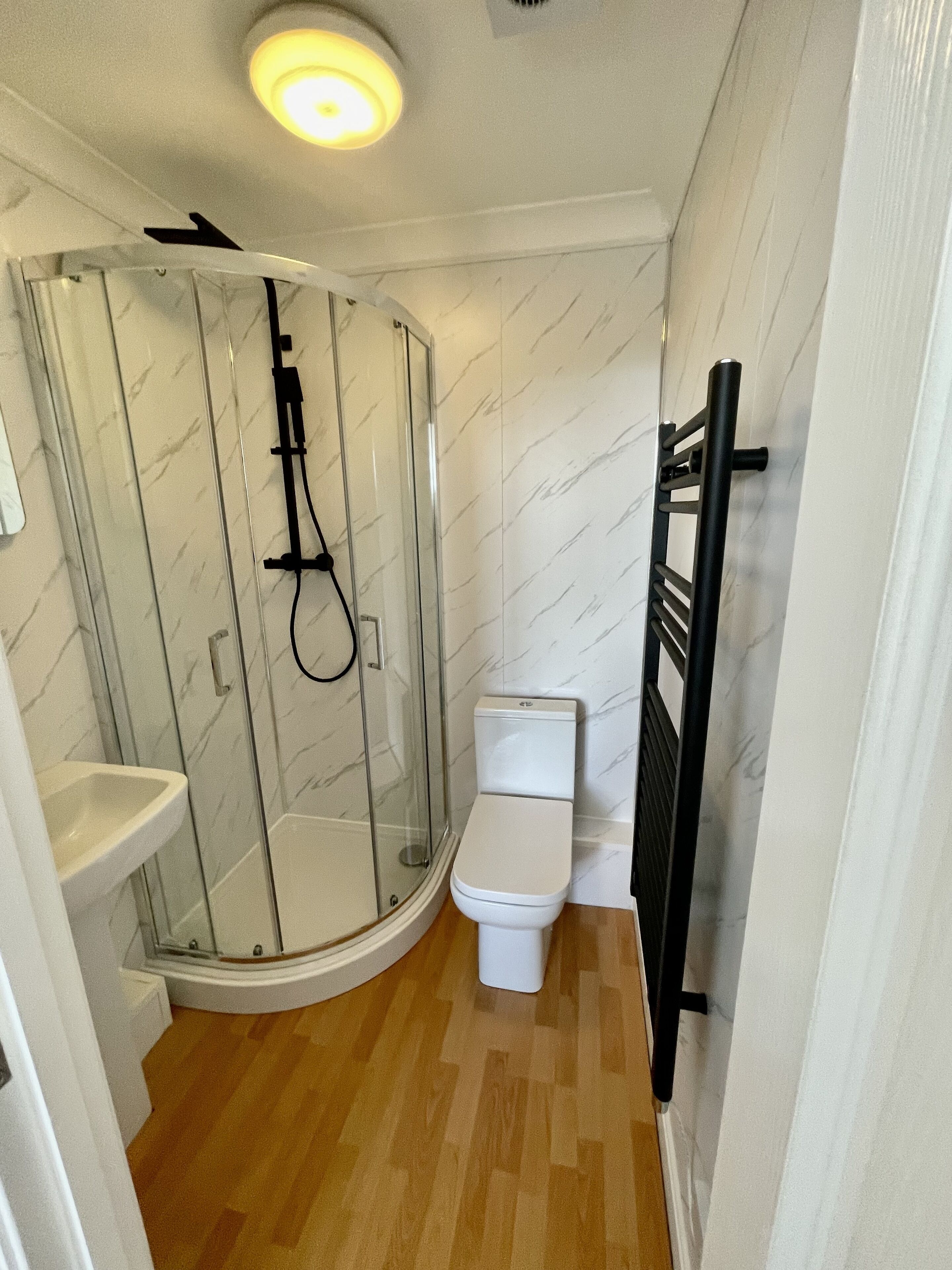 Een badkamer met een douchecabine van glas, een wit toilet en een houten vloer.