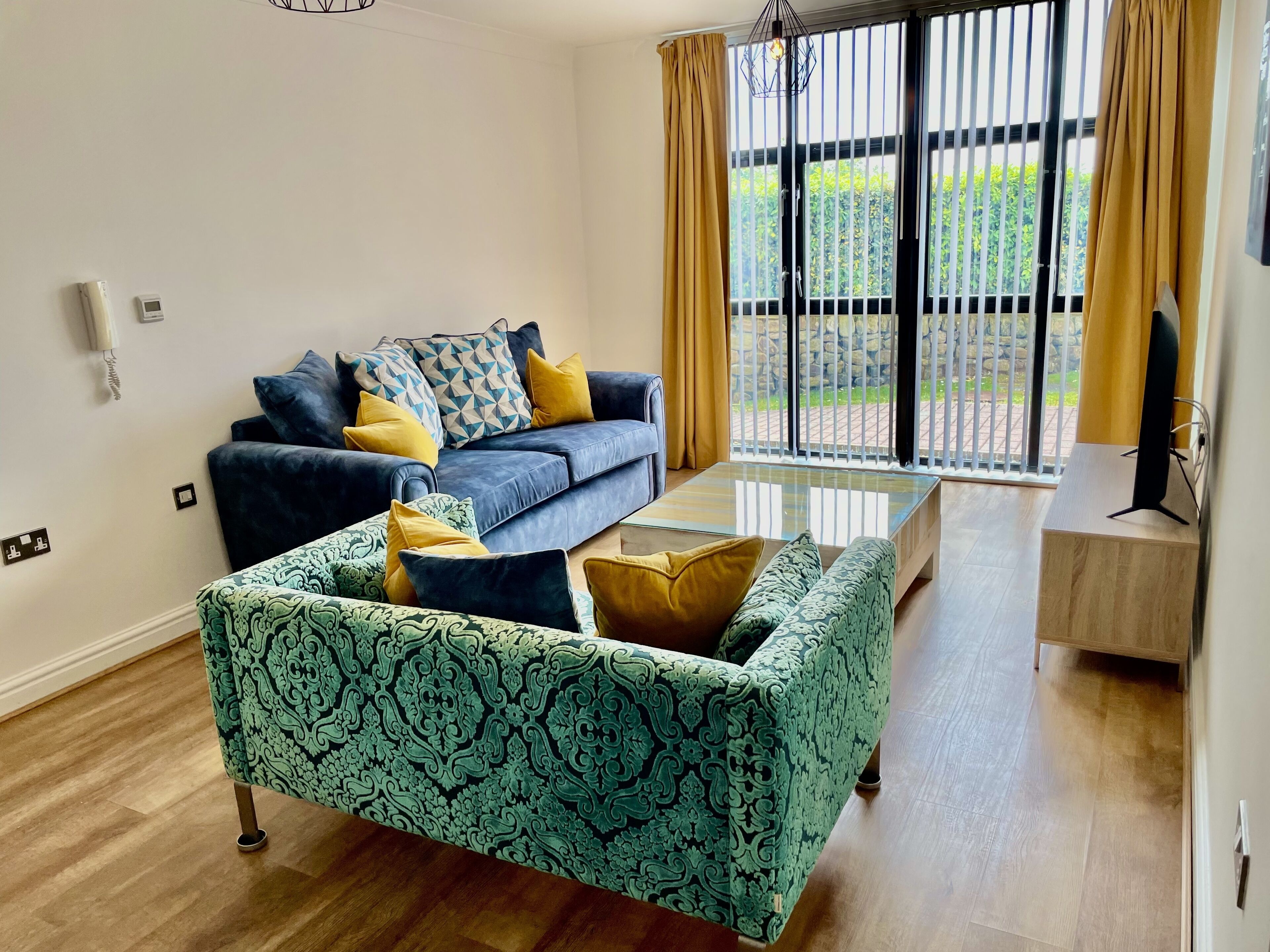 A living room with a blue sofa, patterned armchair, and a glass coffee table.