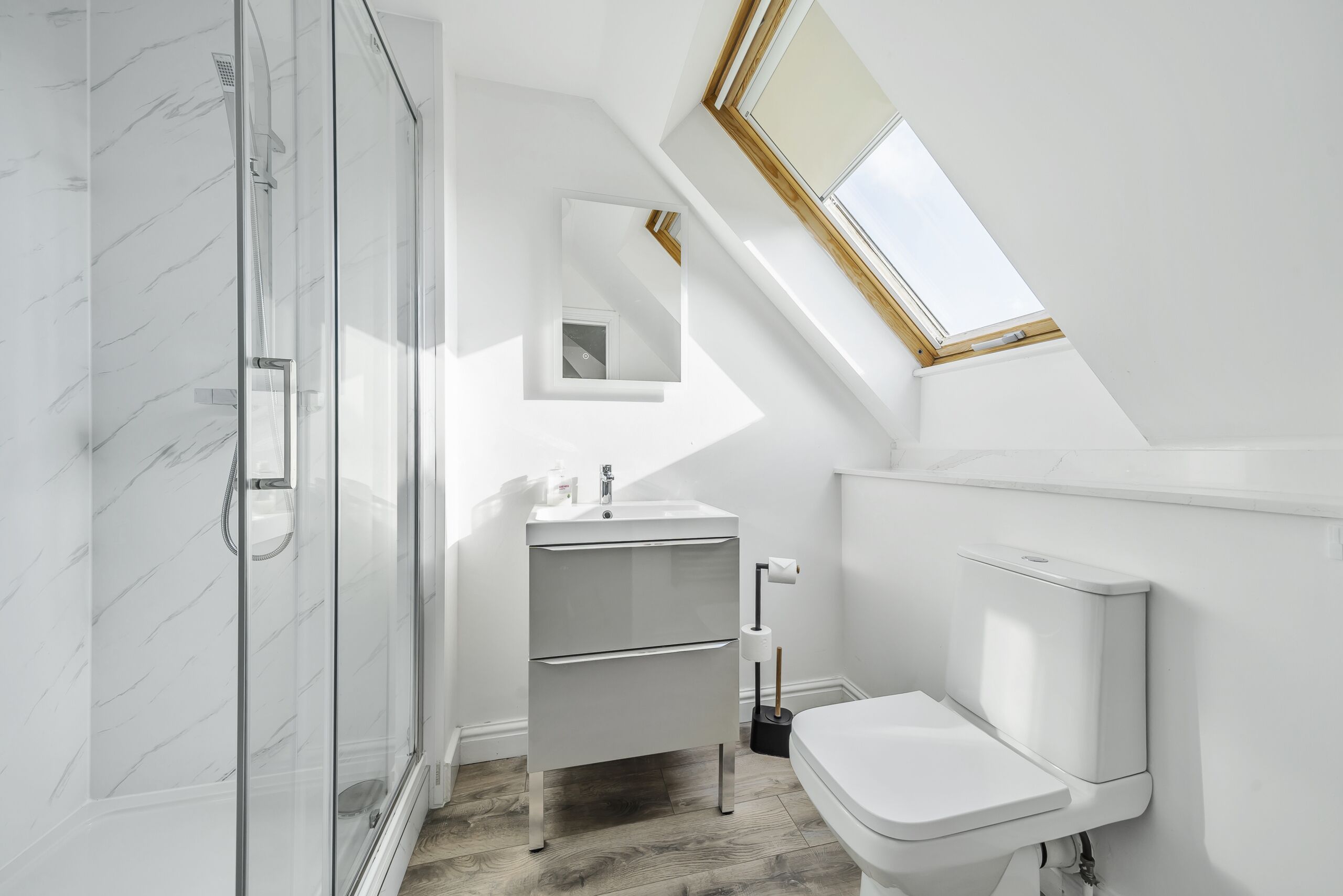 A modern bathroom with a glass shower enclosure, a white sink with a mirror above it, and a toilet.