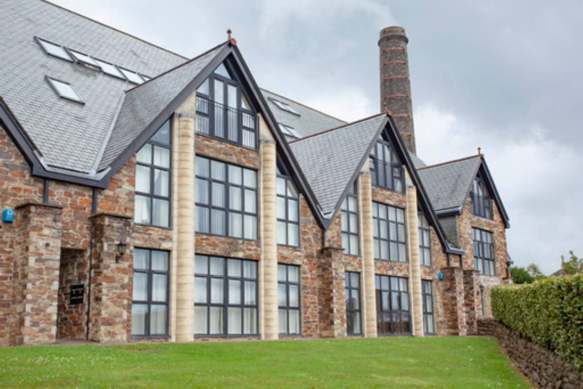 A large, multi-story building with a stone facade, large windows, and a prominent chimney.