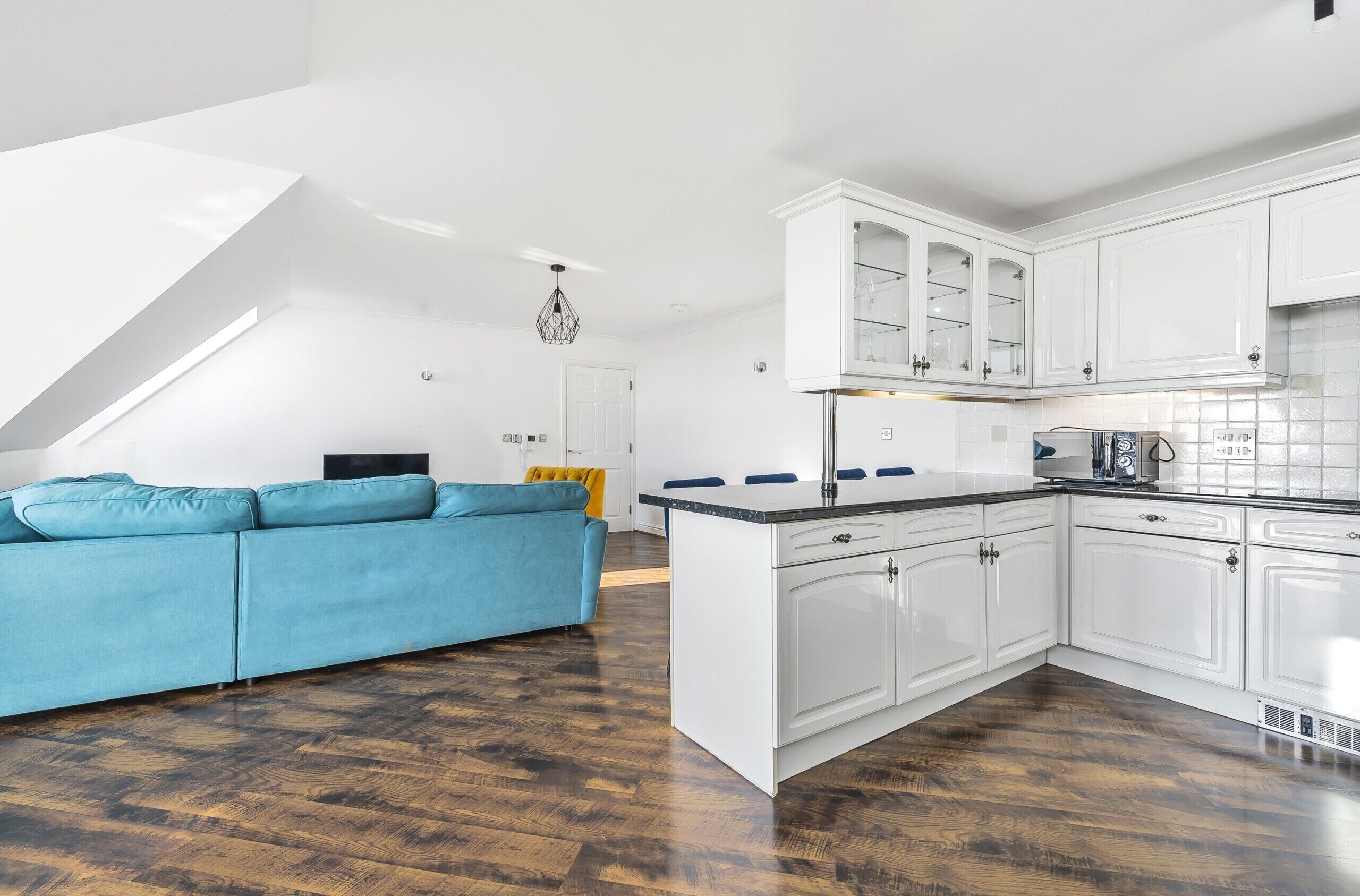 Una cocina moderna con armarios blancos, un sofá azul y suelo de madera.