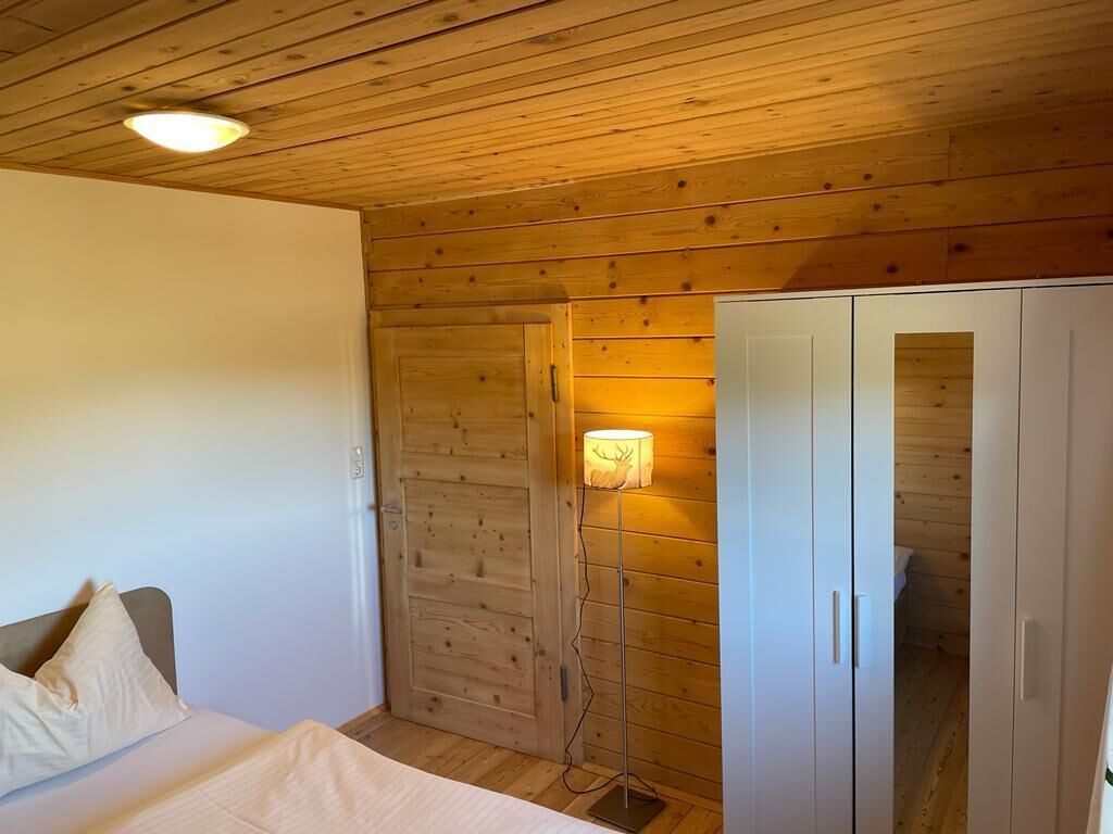 A room with wooden walls, a bed with pillows, a bedside table, and a wardrobe.