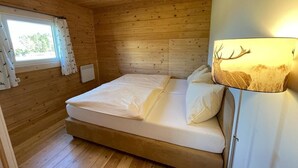 A wooden cabin room with a bed, a window with curtains, and a lamp with a deer head shade. - Waldchalet am Eichhof (Natters)