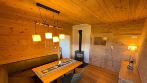 A cozy wooden cabin interior with a dining table, chairs, a bench, a fireplace, and hanging lights. - Waldchalet am Eichhof (Natters)