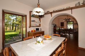 Comedor con una mesa de mármol, sillas, frutero y cocina al fondo.