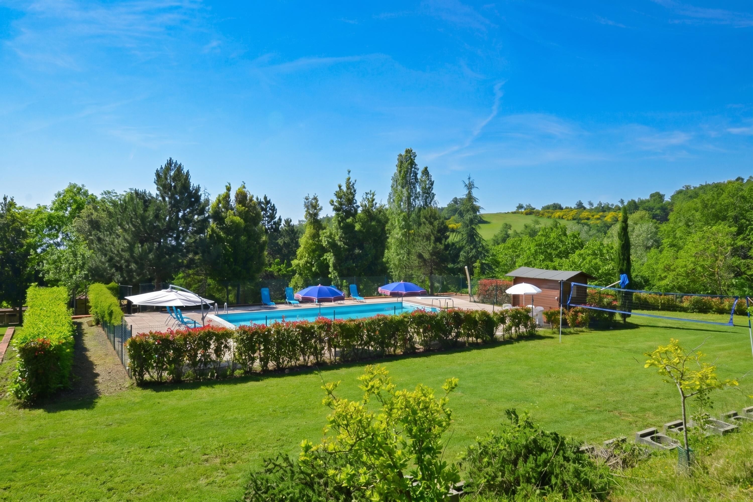 Un espace piscine agrémenté de parasols, un petit bâtiment et une pelouse bien entretenue.