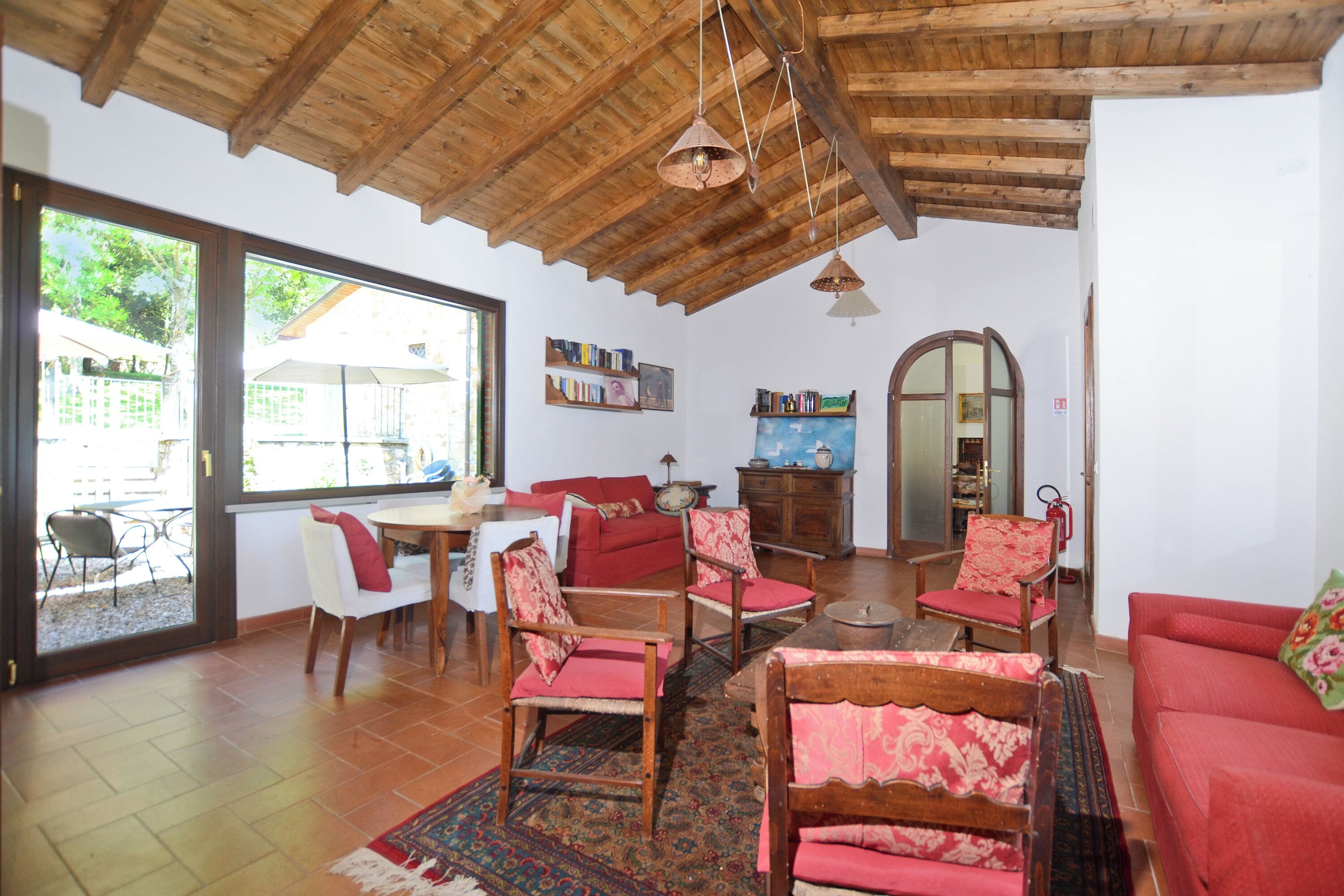 A spacious living area with a wooden ceiling, a dining table, red sofas, and a large window.