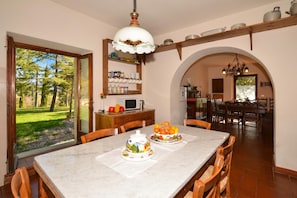 Un comedor con una mesa de mármol, sillas, un frutero y una cocina al fondo.