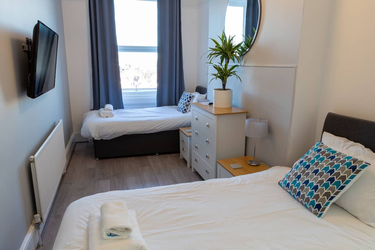 A hotel room with two beds, a dresser, a TV, a potted plant, and a window with curtains.