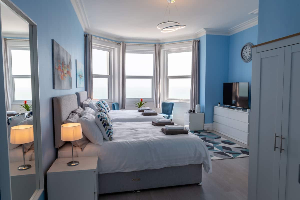 A modern bedroom with two beds, a TV, and a large window.