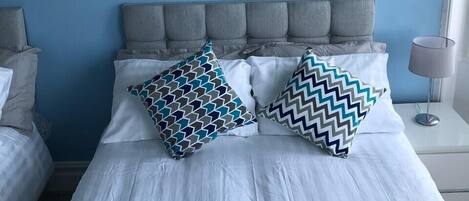 A bedroom with a bed, two pillows, a nightstand, a lamp, and a painting on the wall.