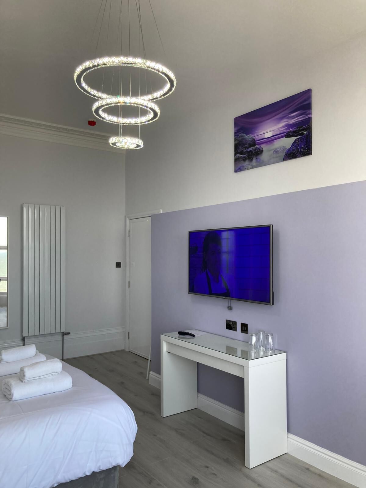 A modern bedroom with a bed, a desk, a TV, and a painting on the wall.