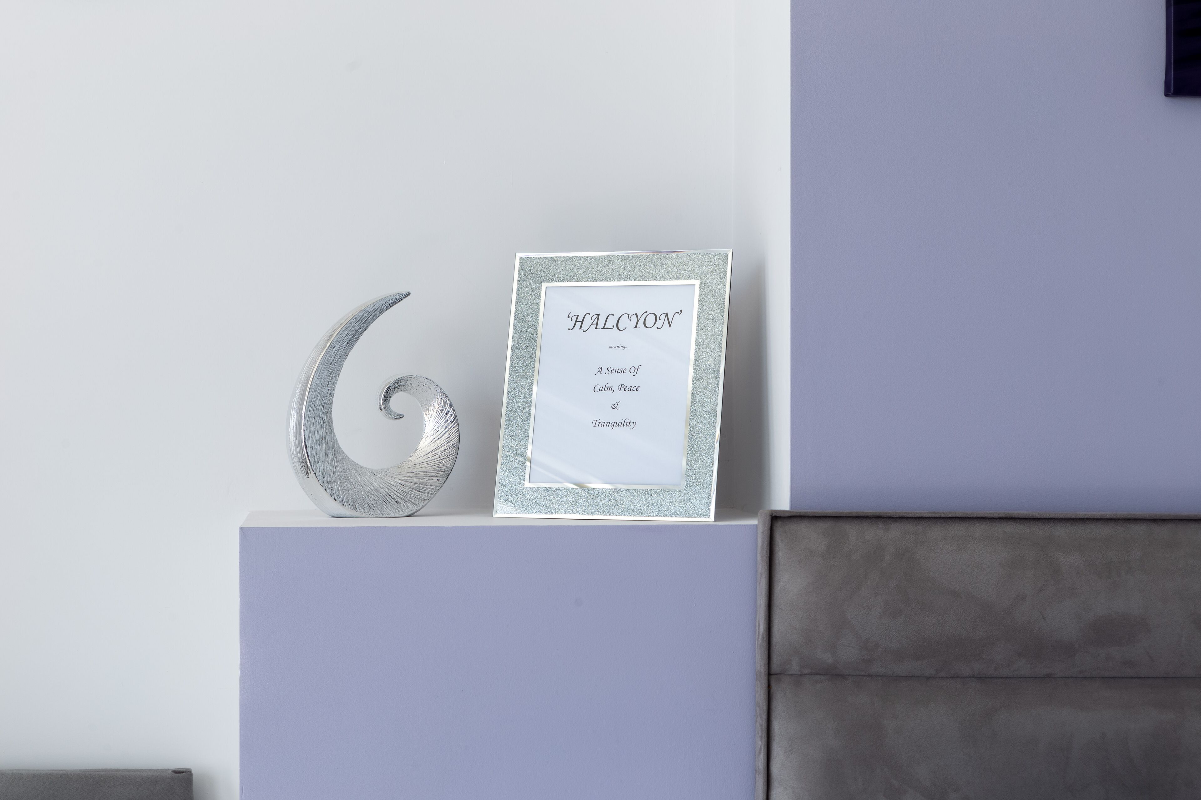 Un letrero enmarcado con el texto 'HALCYON' y 'Una sensación de calma, paz y tranquilidad' sobre un pedestal blanco, frente a una pared.