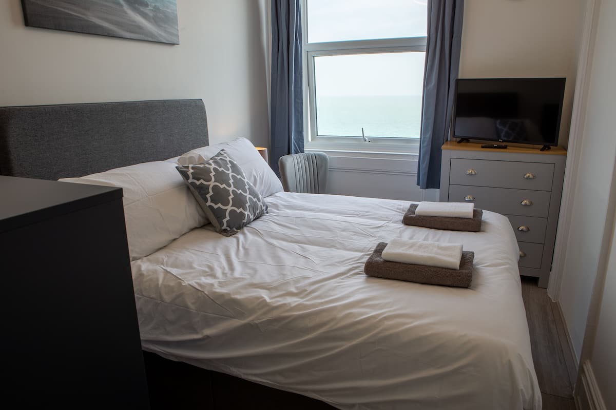 A neatly made bed with pillows and a flat-screen TV on a dresser.