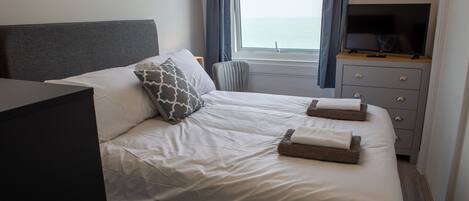 Una cama bien hecha con almohadas y un televisor de pantalla plana sobre un tocador.