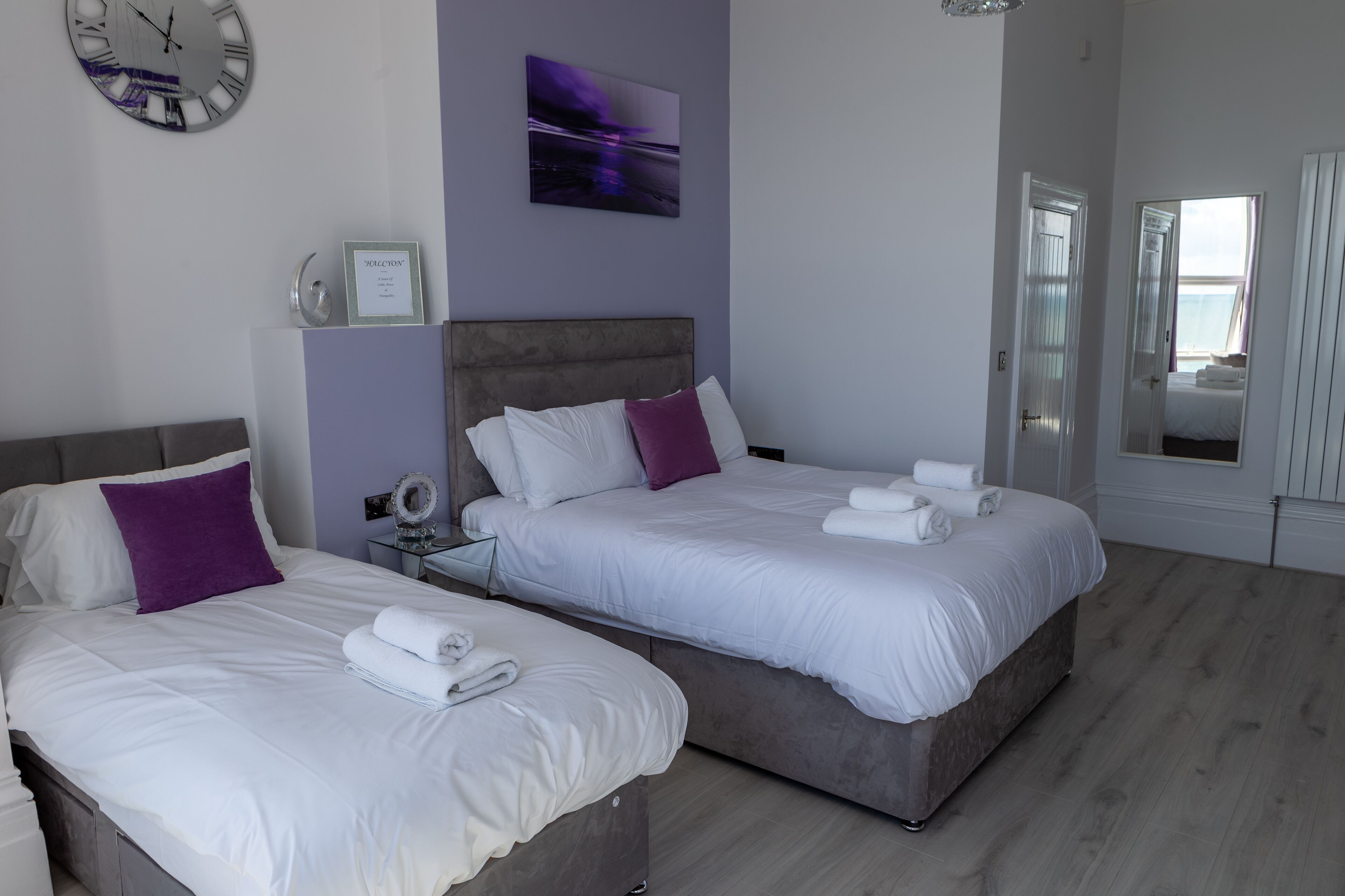 A hotel room with two beds, a clock, a framed certificate, and a painting on the wall.