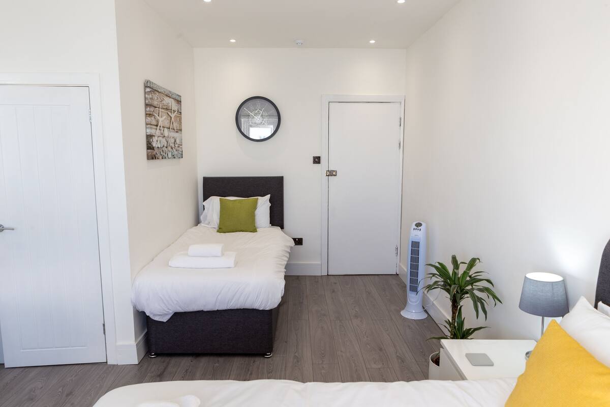 A modern bedroom with a bed, bedside table, lamp, and a wall clock.