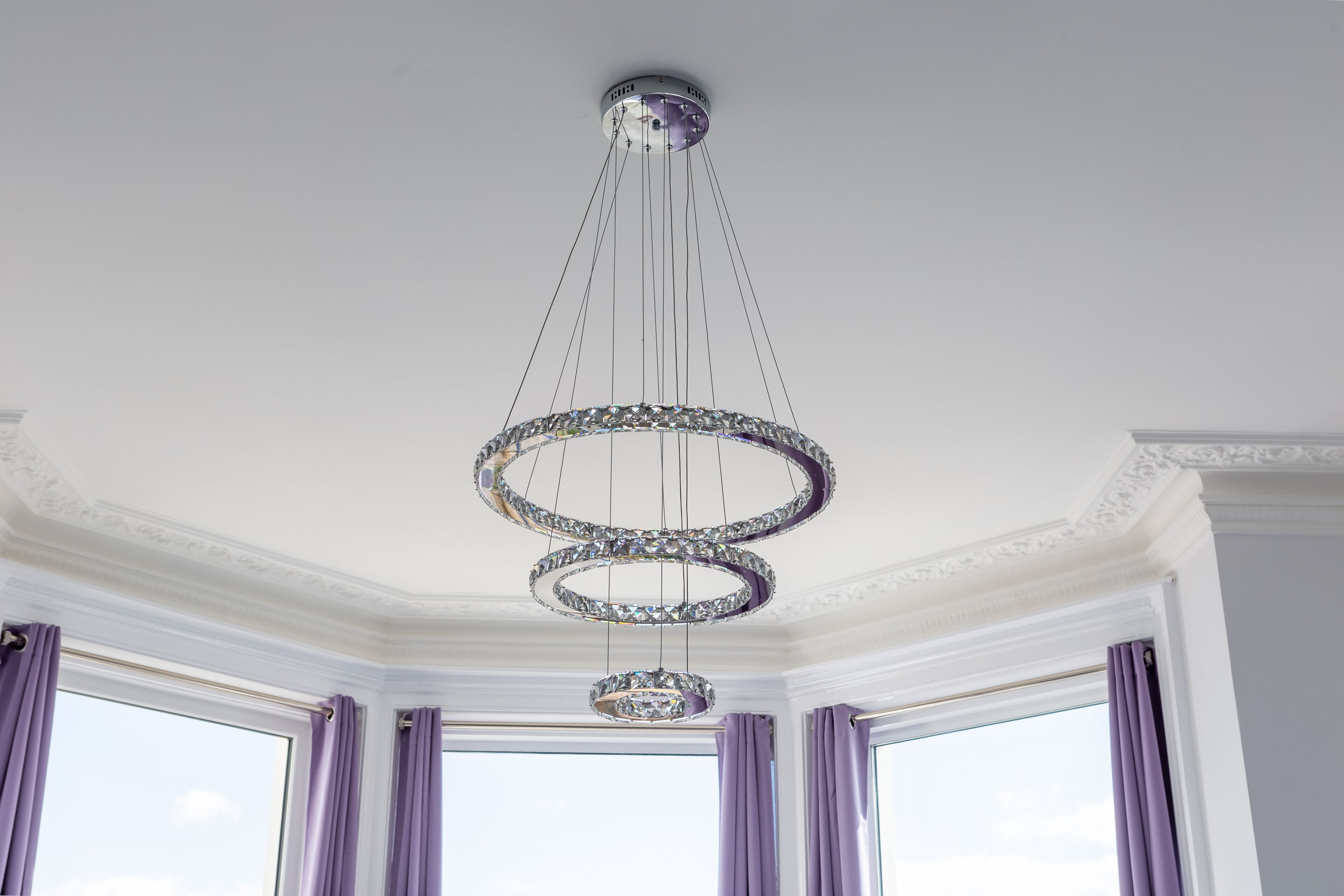A chandelier with multiple tiers and crystal decorations in a room with large windows and purple curtains.