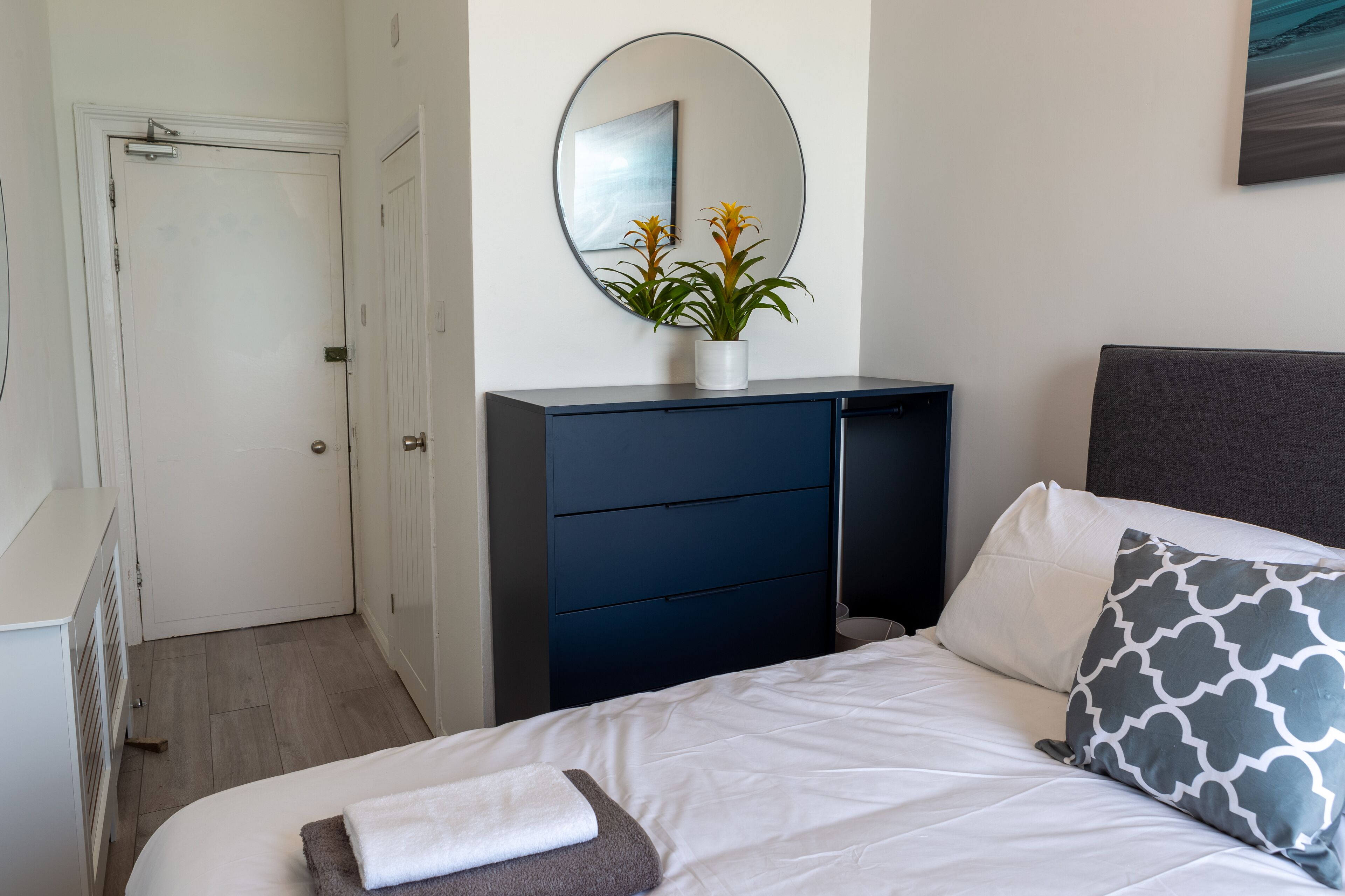 Un dormitorio con cama, cómoda, espejo y planta en maceta.