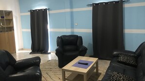 A living room with a blue wall, two black leather sofas, a black leather armchair, a wooden coffee table, and a patterned rug. - Blue Residence (Bakau)