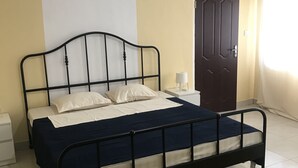 A bedroom with a bed, bedside table, and a door. - Blue Residence (Bakau)