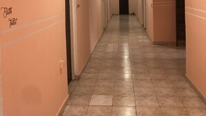 A long, narrow hallway with pink walls and tiled flooring, leading to a dark door at the end. - Blue Residence (Bakau)