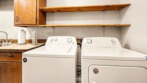 A laundry area with two white washing machines, wooden cabinets, and a countertop with a sink.