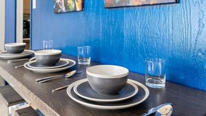 A dining table set with bowls, plates, and cutlery, against a blue wall with abstract art.