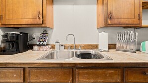 A kitchen with wooden cabinets, a double sink, a coffee maker, a knife block, and a toaster.
