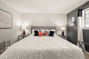 Habitación de hotel ordenada con una cama grande, dos mesitas de noche y una ventana con cortinas.