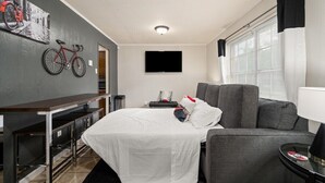 Moderni hotellihuone, jossa on sänky, harmaa sohva, televisio ja pyörä seinällä.