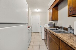Una cocina compacta con electrodomésticos blancos, encimera de granito, armarios de madera y suelo de baldosas.