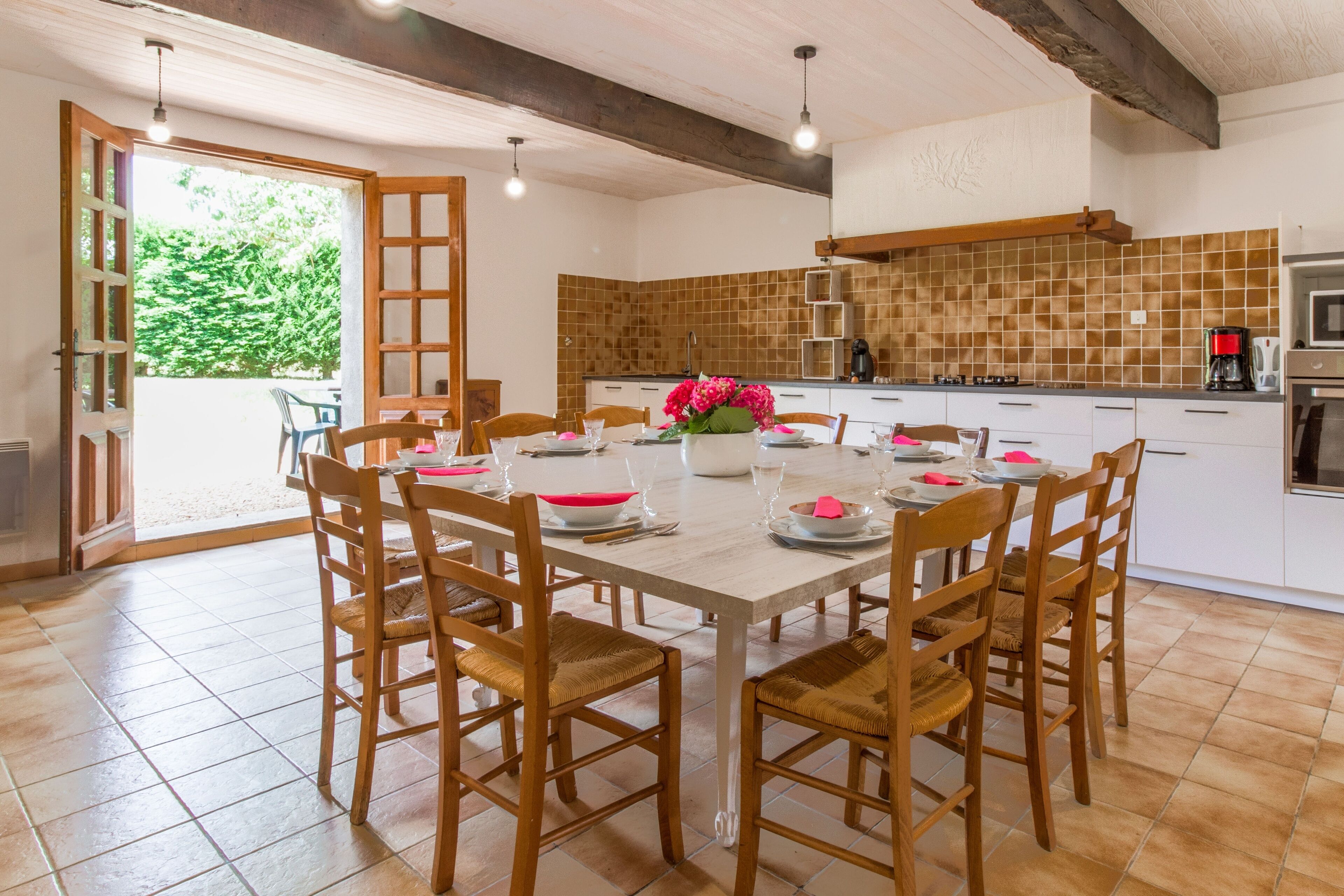 Un coin repas avec une table et des chaises en bois, une cuisine avec un dosseret carrelé et une vue sur la verdure à l’extérieur.