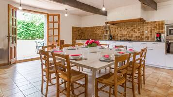 Un coin repas avec une table et des chaises en bois, une cuisine avec un dosseret carrelé et une vue sur la verdure à l’extérieur.
