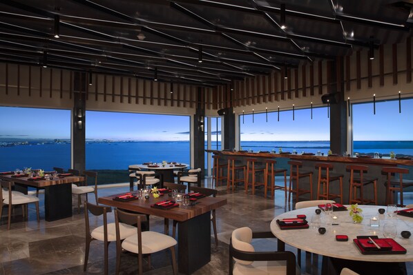 Un restaurant moderne offrant une vue panoramique sur la mer, avec plusieurs tables et un bar.