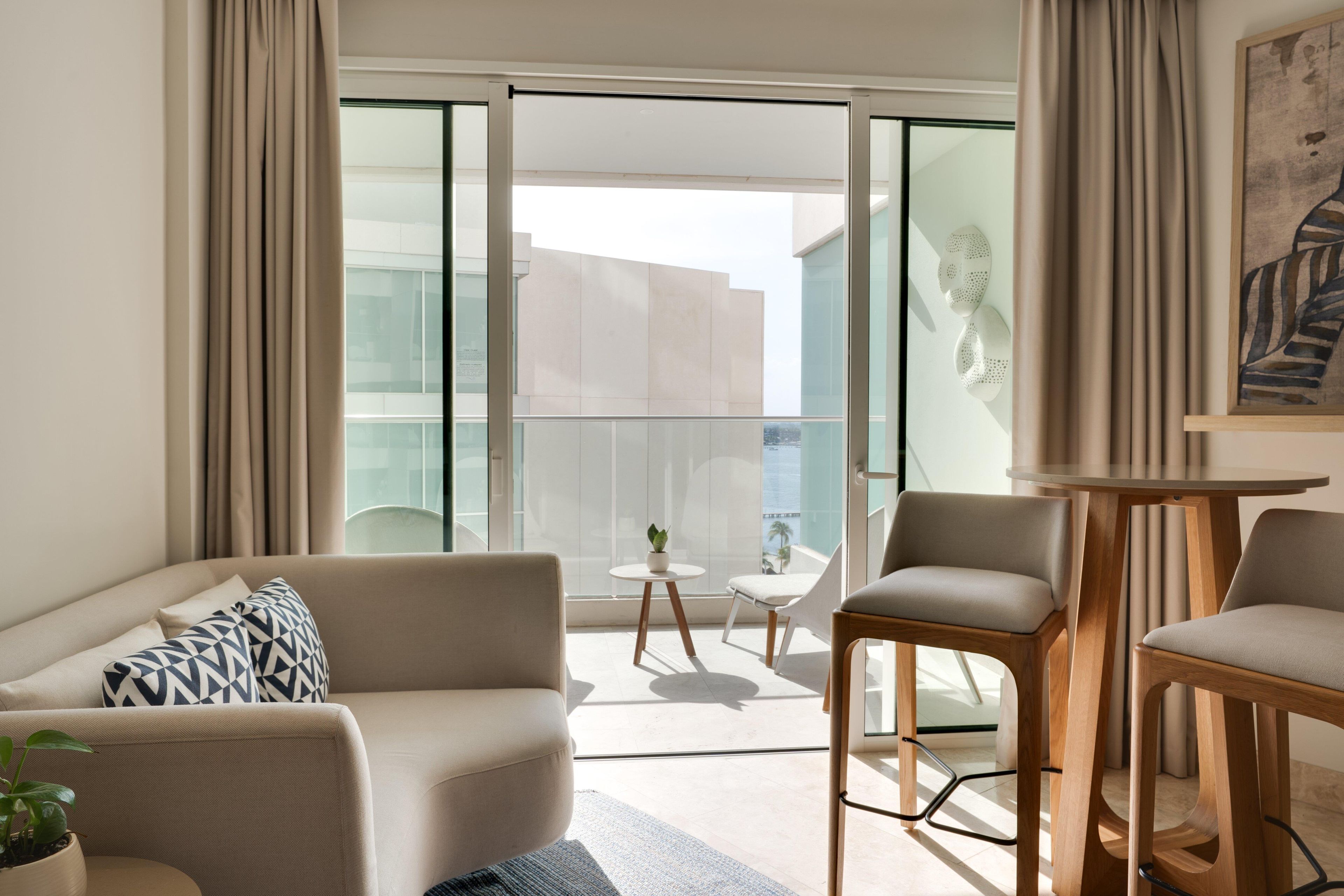 A modern living room with a sofa, two chairs, a small table, and a large window with a view of buildings.