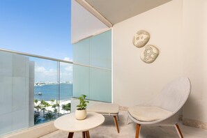 Un balcon avec vue sur la mer, une table ronde agrémentée d’une plante, un banc rembourré et deux éléments décoratifs fixés au mur.