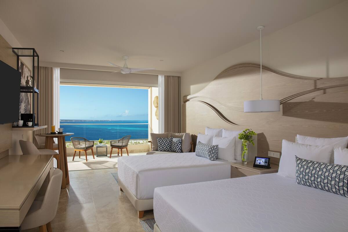 Een hotelkamer met twee bedden, een bureau en uitzicht op zee.