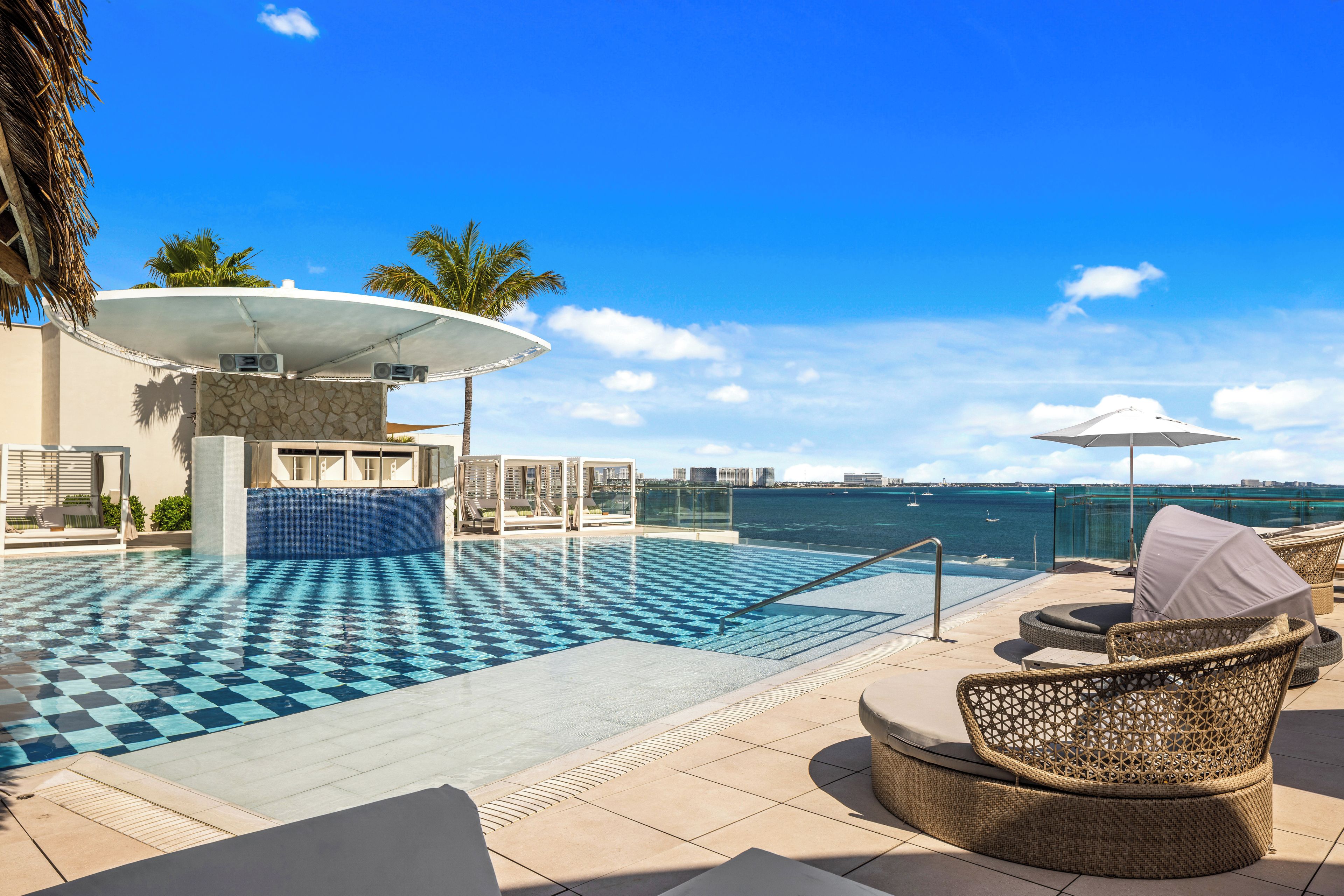 A poolside area with lounge chairs, a covered seating area, and a view of the ocean.