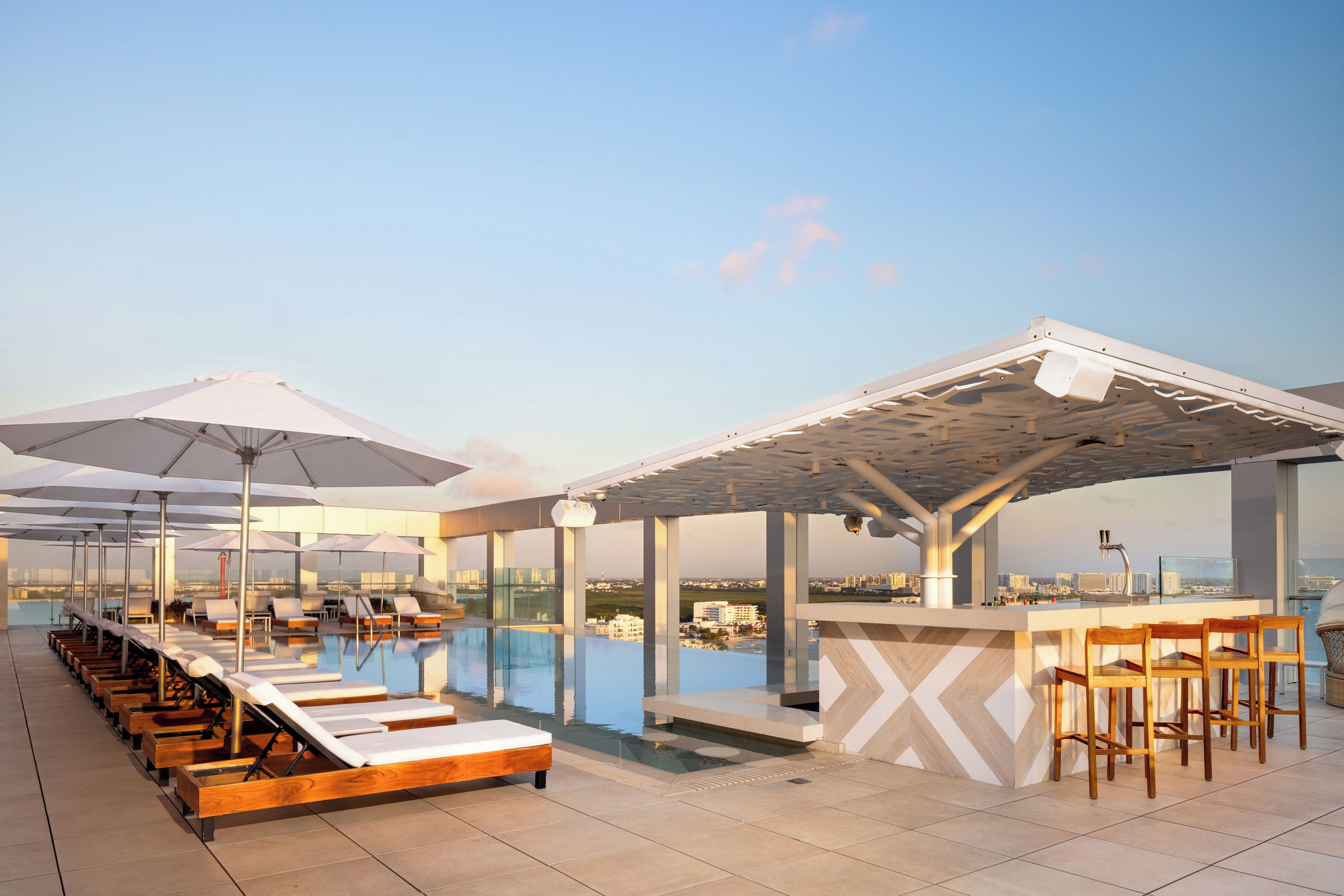 A rooftop pool area with sun loungers, umbrellas, and a bar.