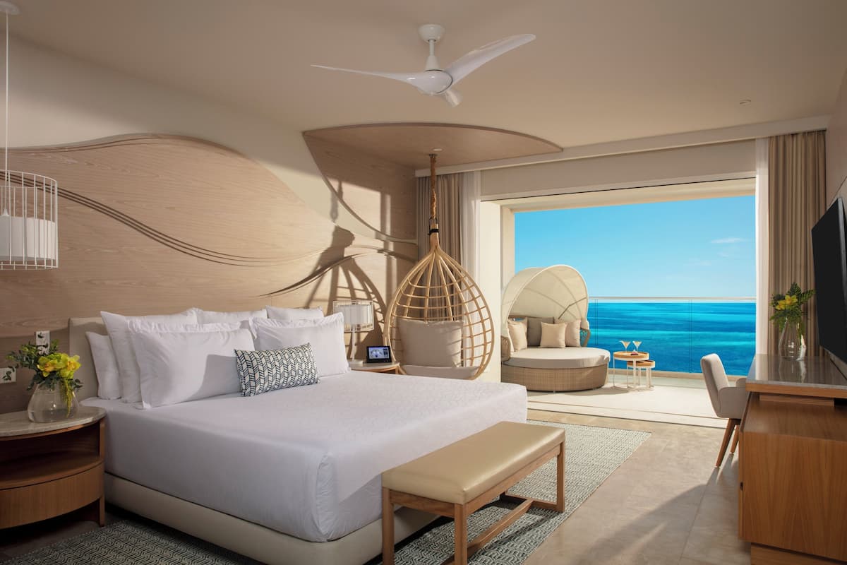 Een moderne hotelkamer met een groot bed, een bureau, een stoel, een plafondventilator en uitzicht op zee.