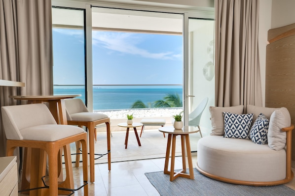 Un salon moderne avec vue sur l’océan, comprenant un canapé, des fauteuils, une petite table et une plante en pot.