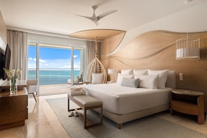 Une chambre d’hôtel moderne avec un grand lit, un bureau, une chaise, une table de chevet, une lampe et une vue sur l’océan.