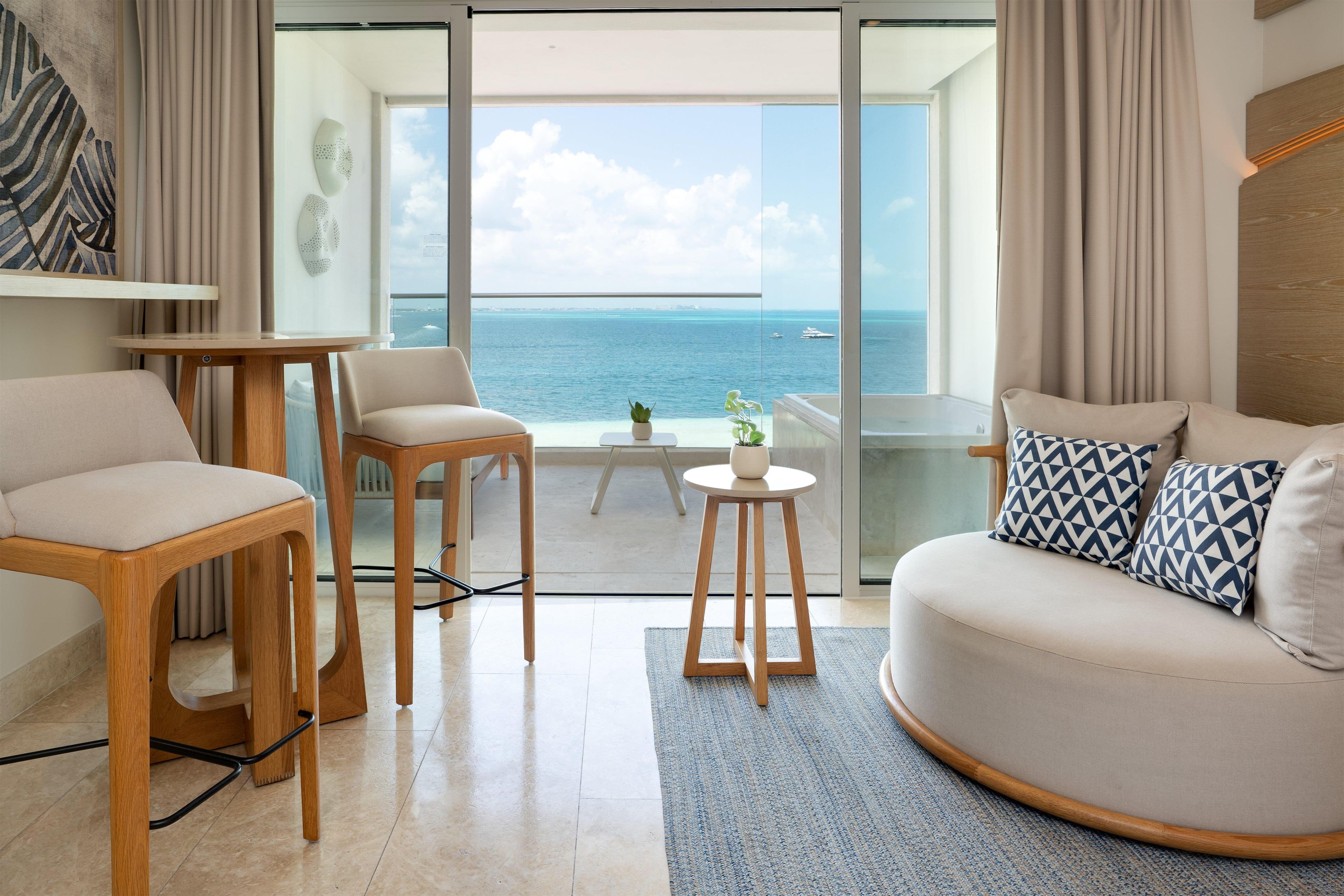 Una sala de estar moderna con vista al mar, que incluye un sofá, sillas, una mesita y una planta en maceta.