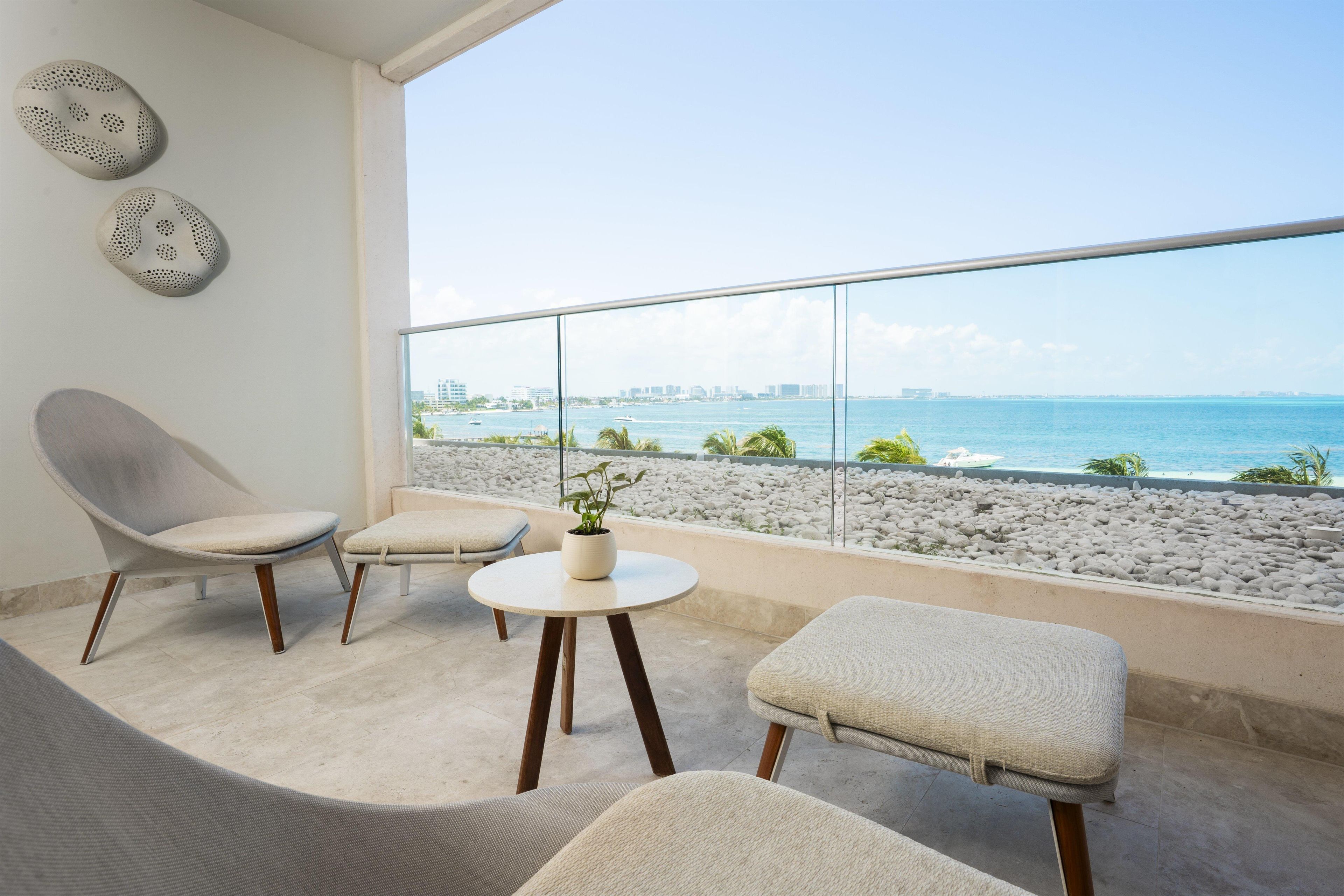 Een balkon met uitzicht op zee, een stoel, een klein tafeltje met een plant en een bank.