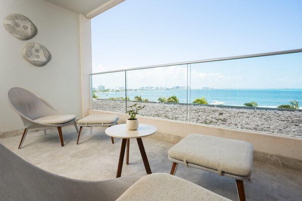 A balcony with a view of the sea, a chair, a small table with a plant, and a sofa.