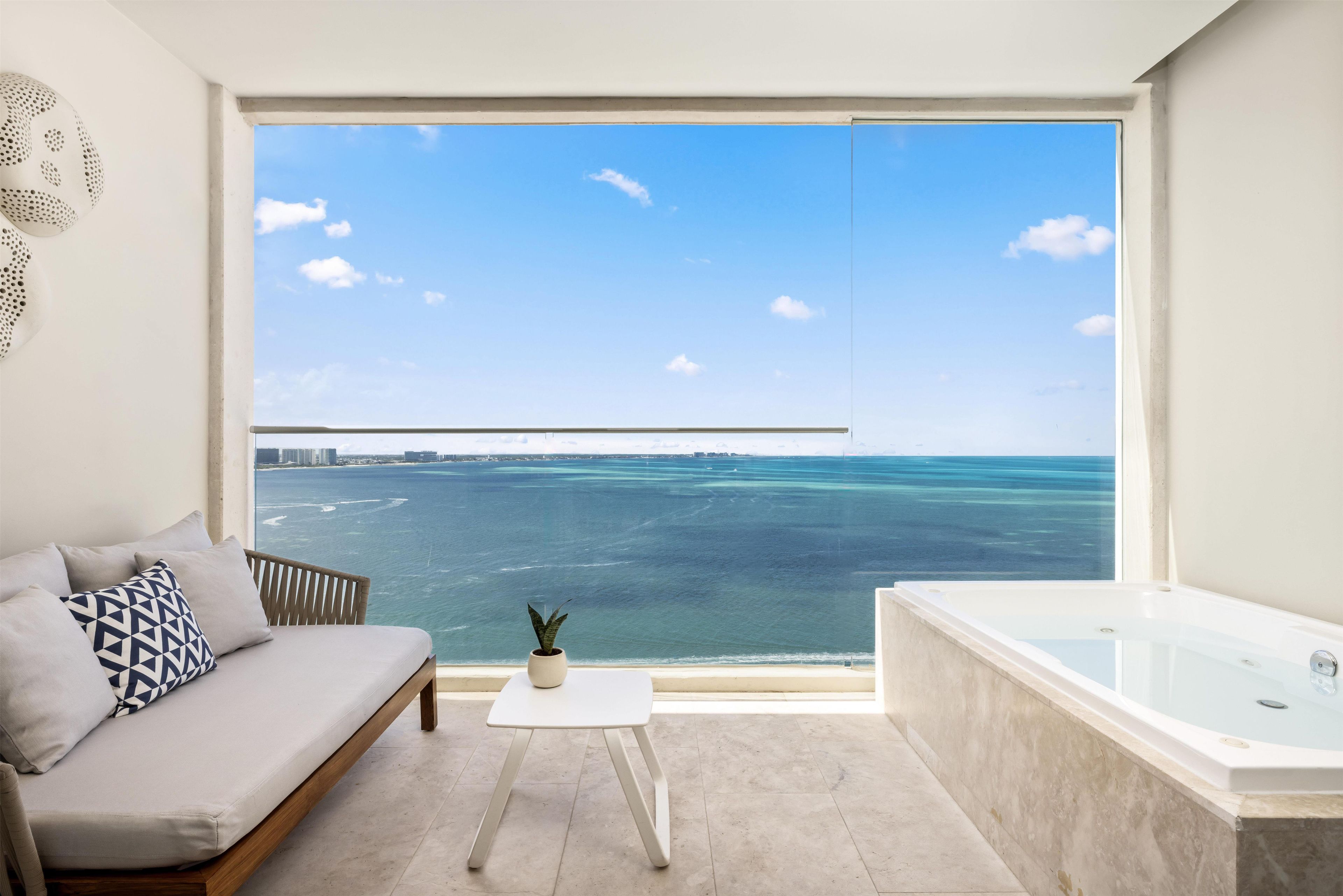 Ein modernes Zimmer mit großem Fenster, einer Couch, einem kleinen Tisch, einem Topf mit Pflanze und einer Badewanne.