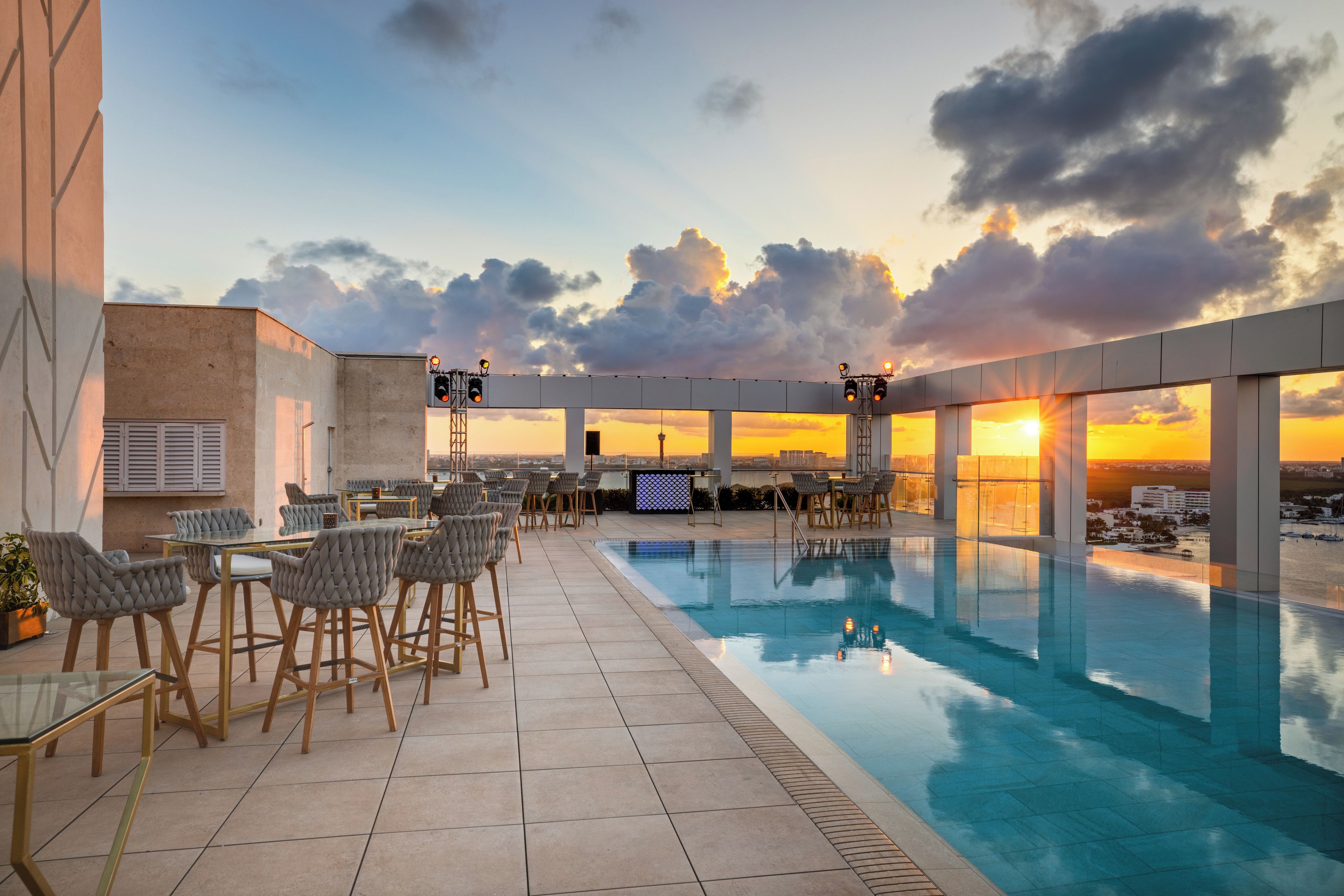 A rooftop pool area with seating and a view of the sunset.